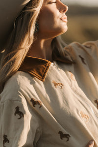 Woman wearing a beige jacket with embroidered designs, standing outdoors.
