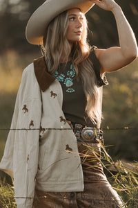 Woman in cowboy hat and western attire standing in a field with barbed wire.