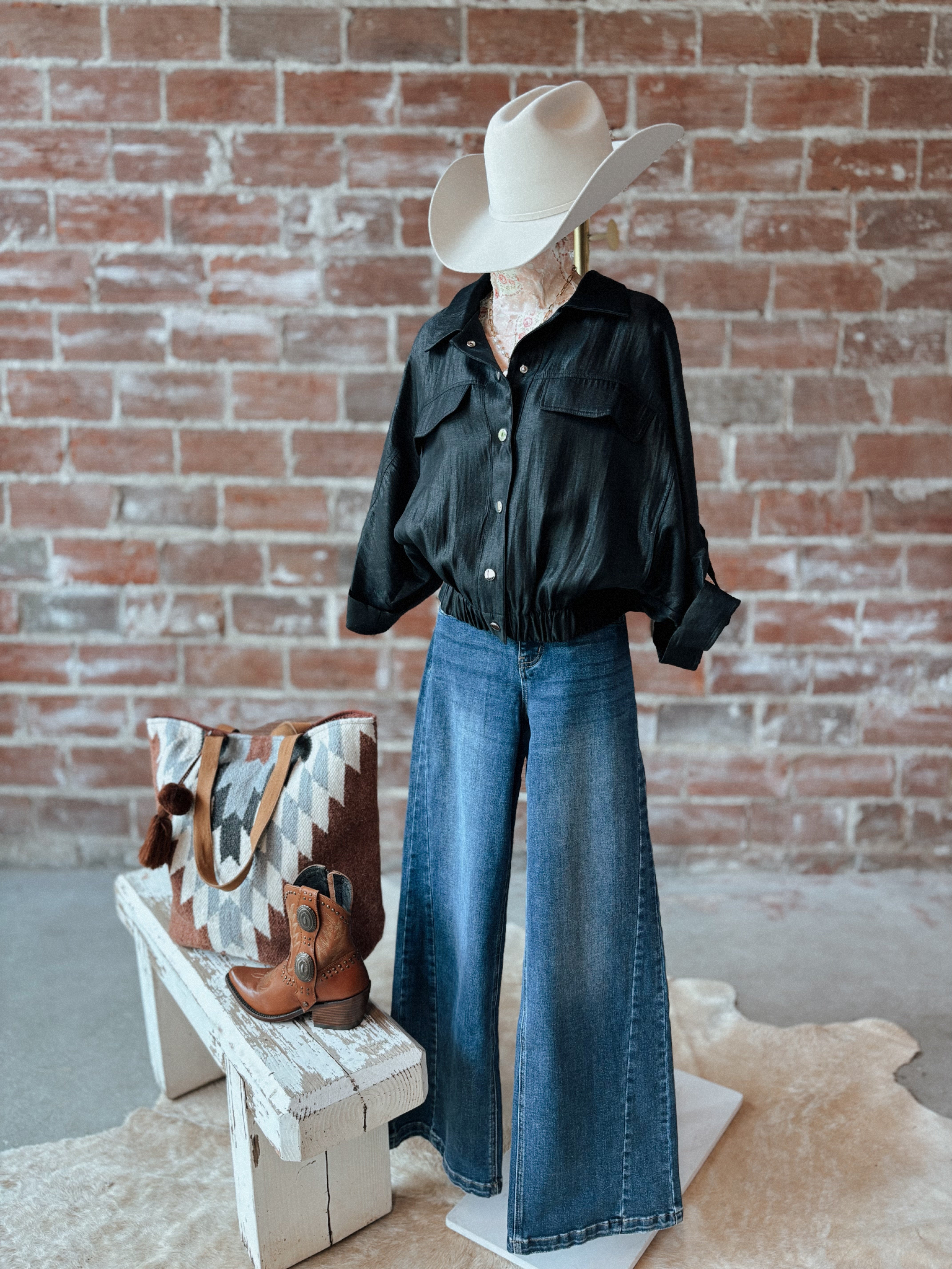 Mannequin wearing a black shirt, blue jeans, and a cowboy hat against a brick wall.