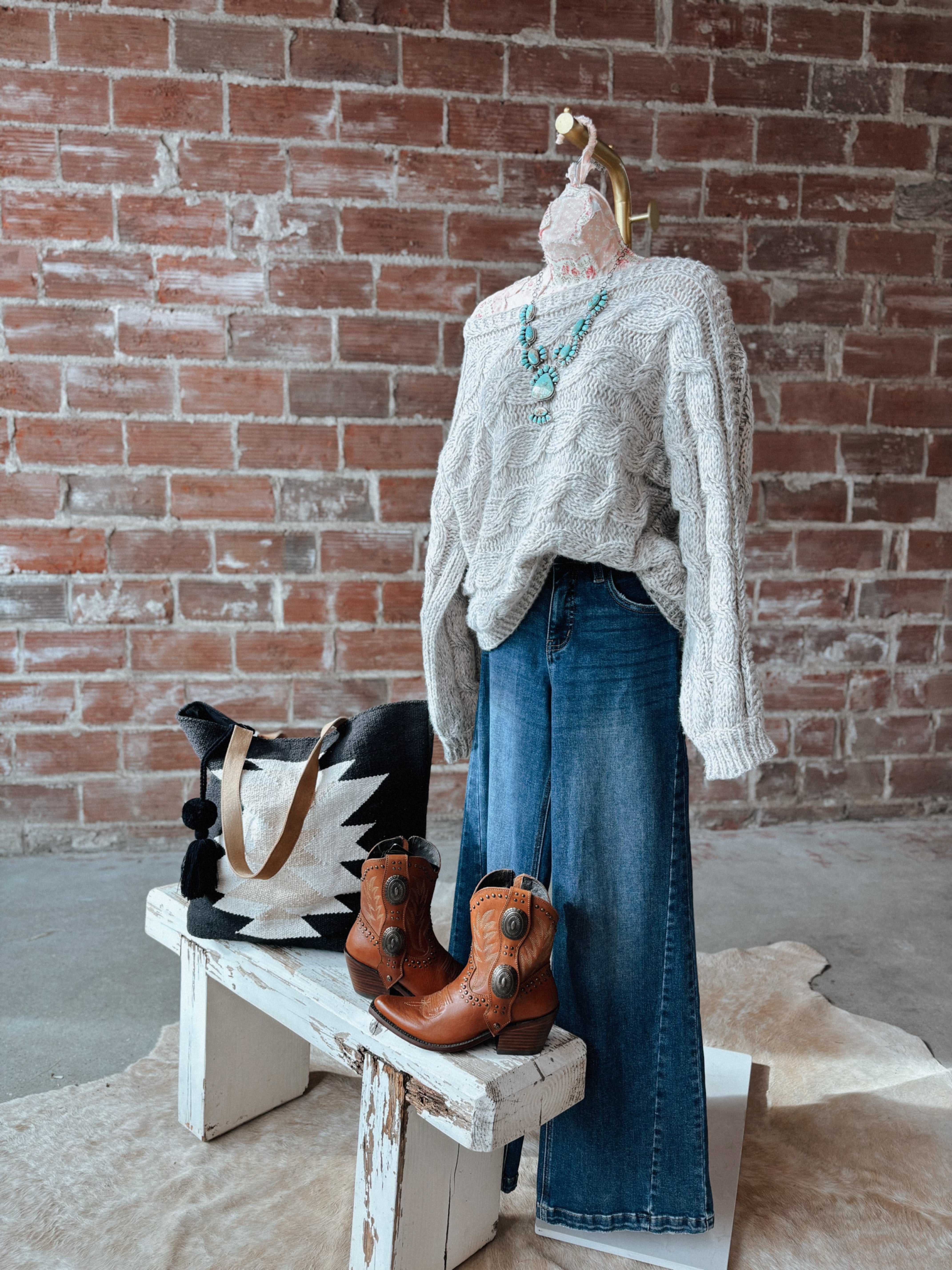 Mannequin wearing a gray sweater and blue jeans with a brick wall background