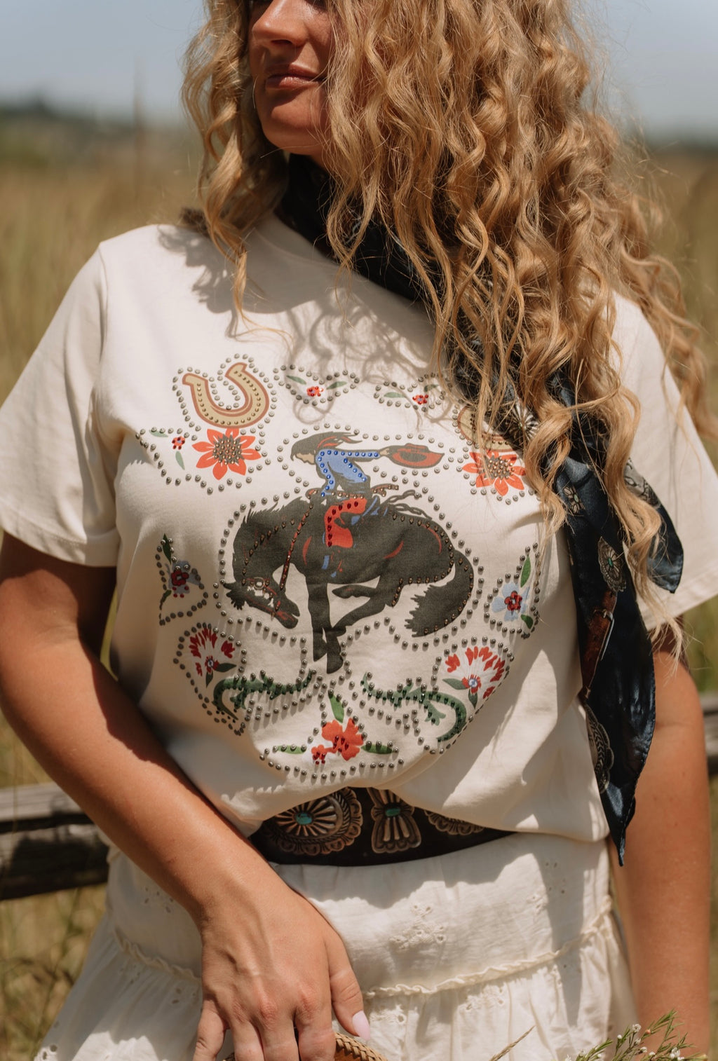 Woman wearing a white t-shirt with a horse and rider design in a field