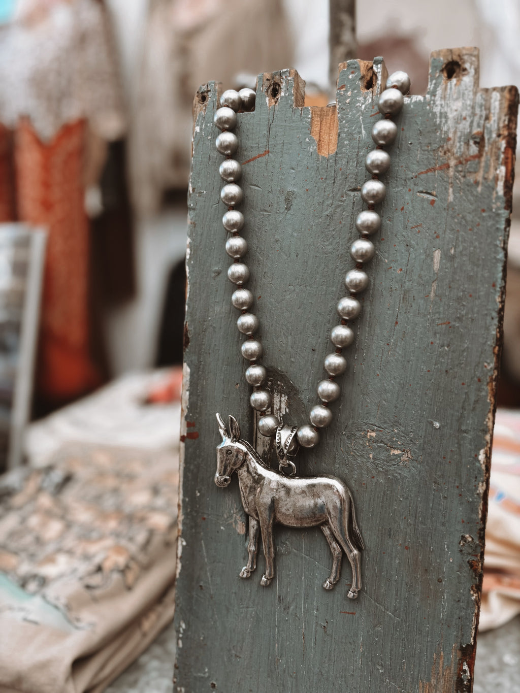 Silver necklace with a donkey pendant on a rustic wooden board.