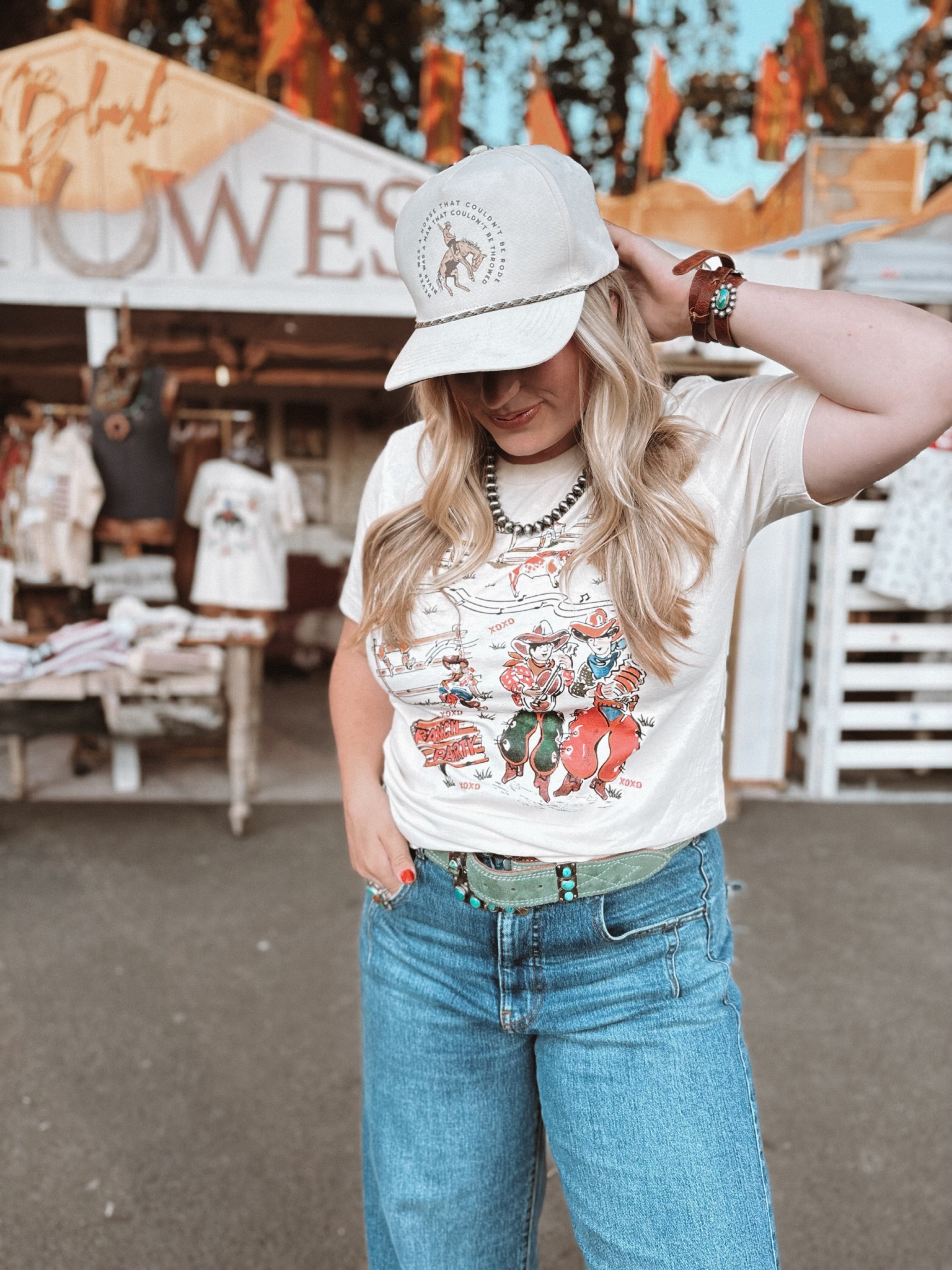 Woman wearing a graphic t-shirt and cap at an outdoor market.