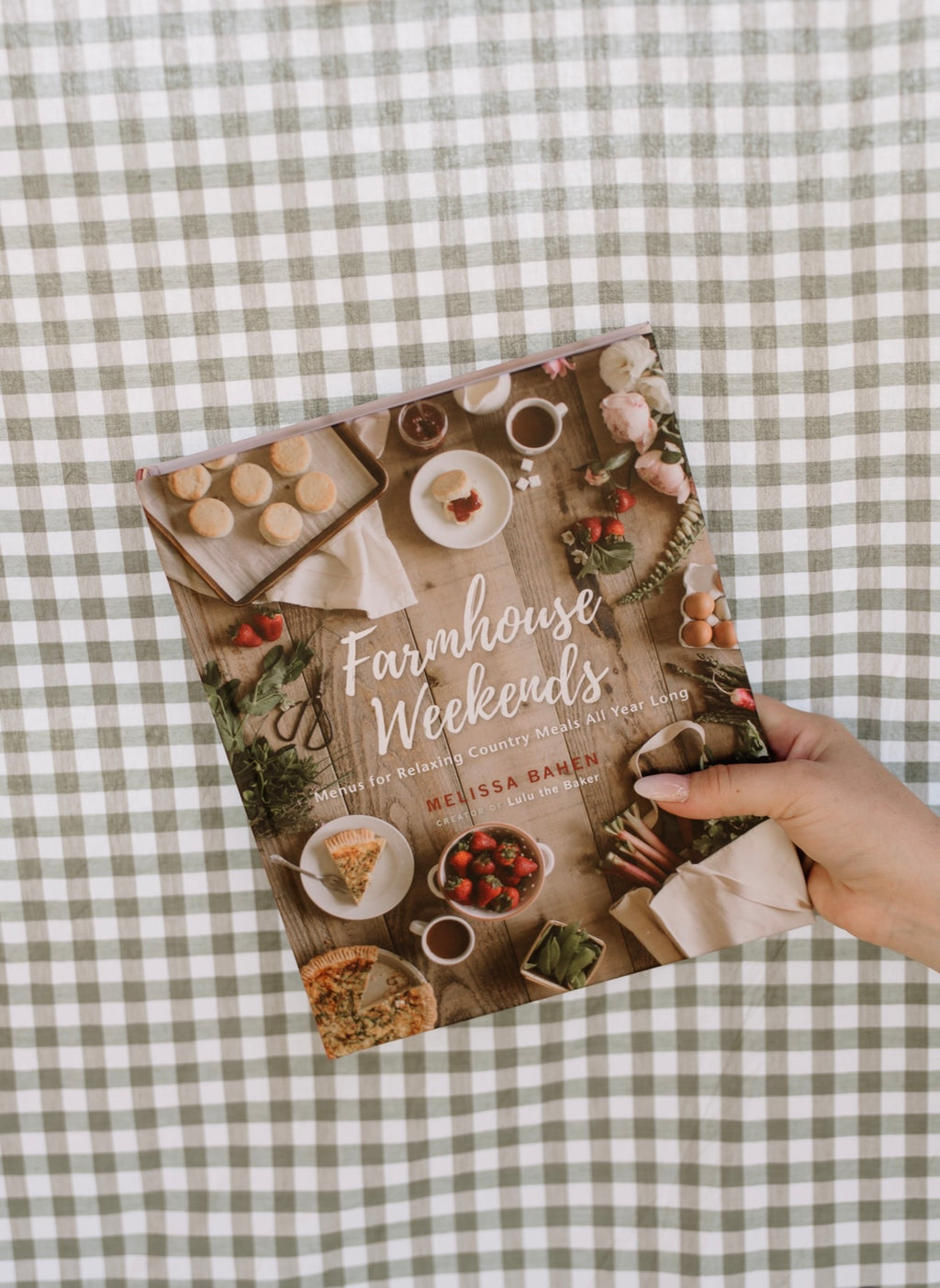 Book titled 'Farmhouse Weekends' held on a checkered tablecloth