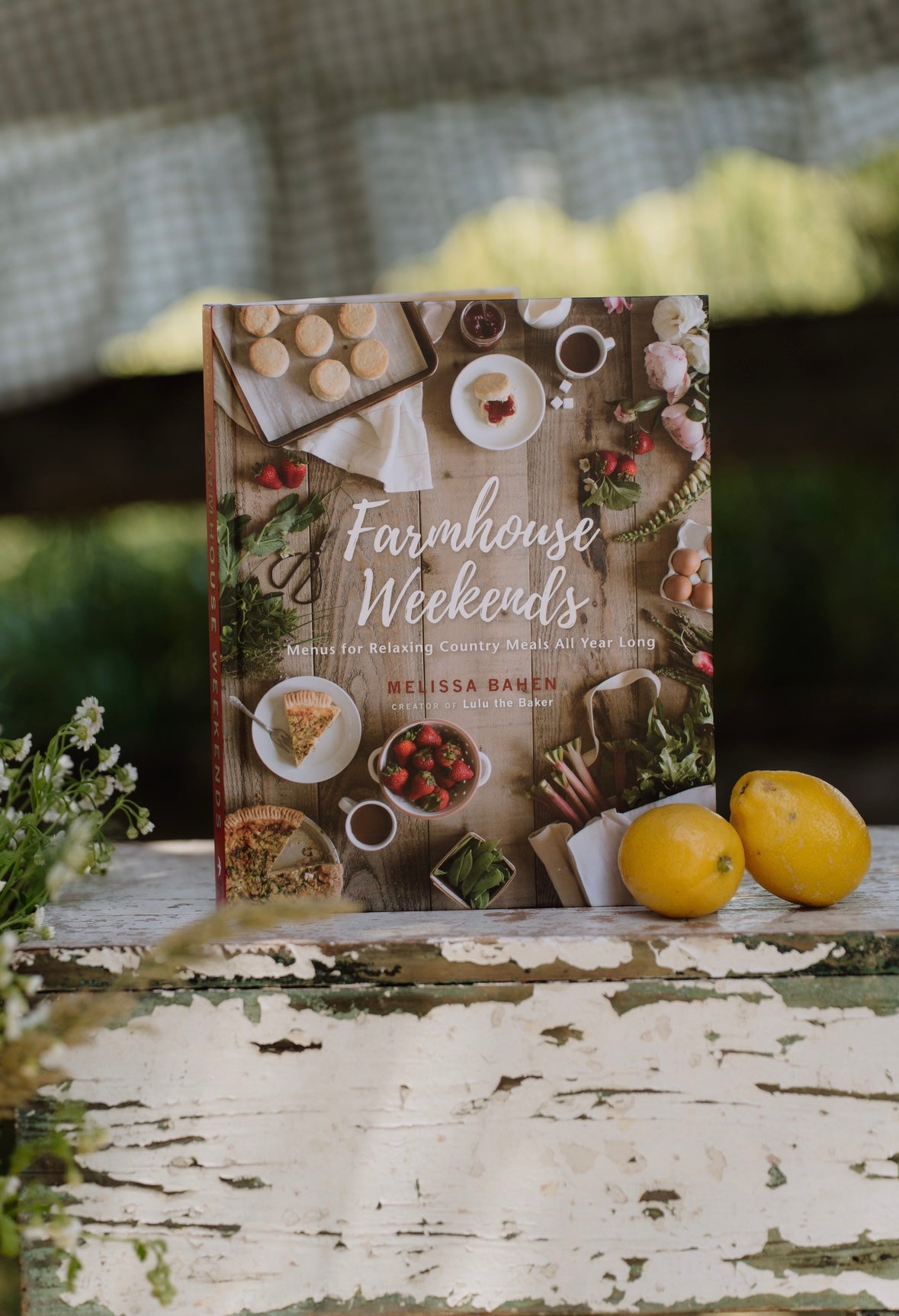 Cookbook titled 'Farmhouse Weekends' on a wooden surface with lemons and greenery.