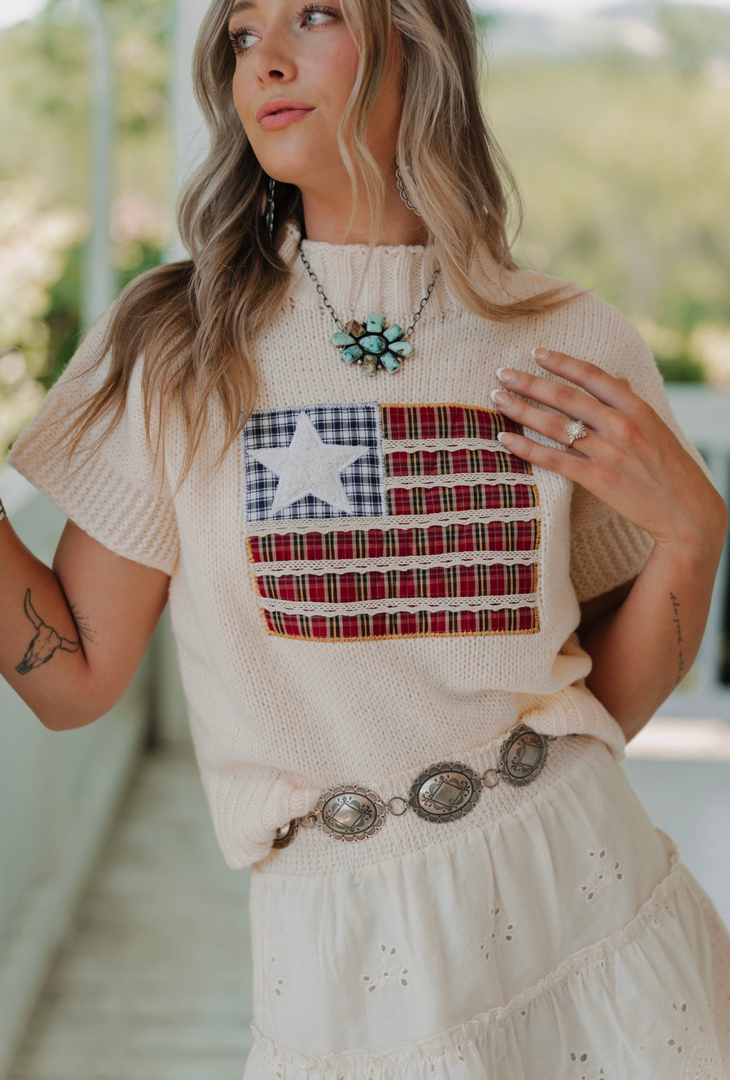Woman wearing a beige sweater with an American flag design outdoors.