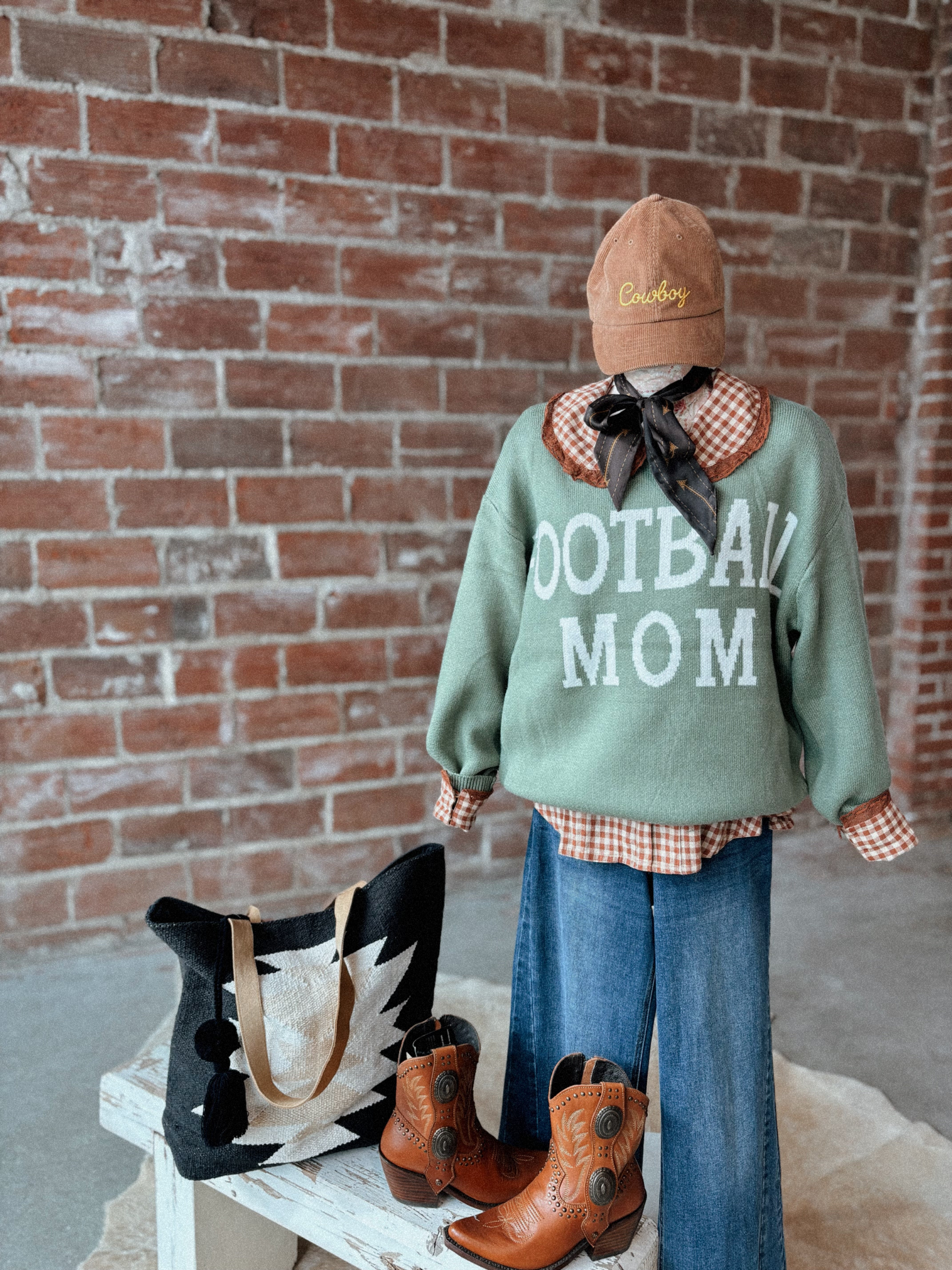 Person wearing a 'Football Mom' sweater with a brick wall background