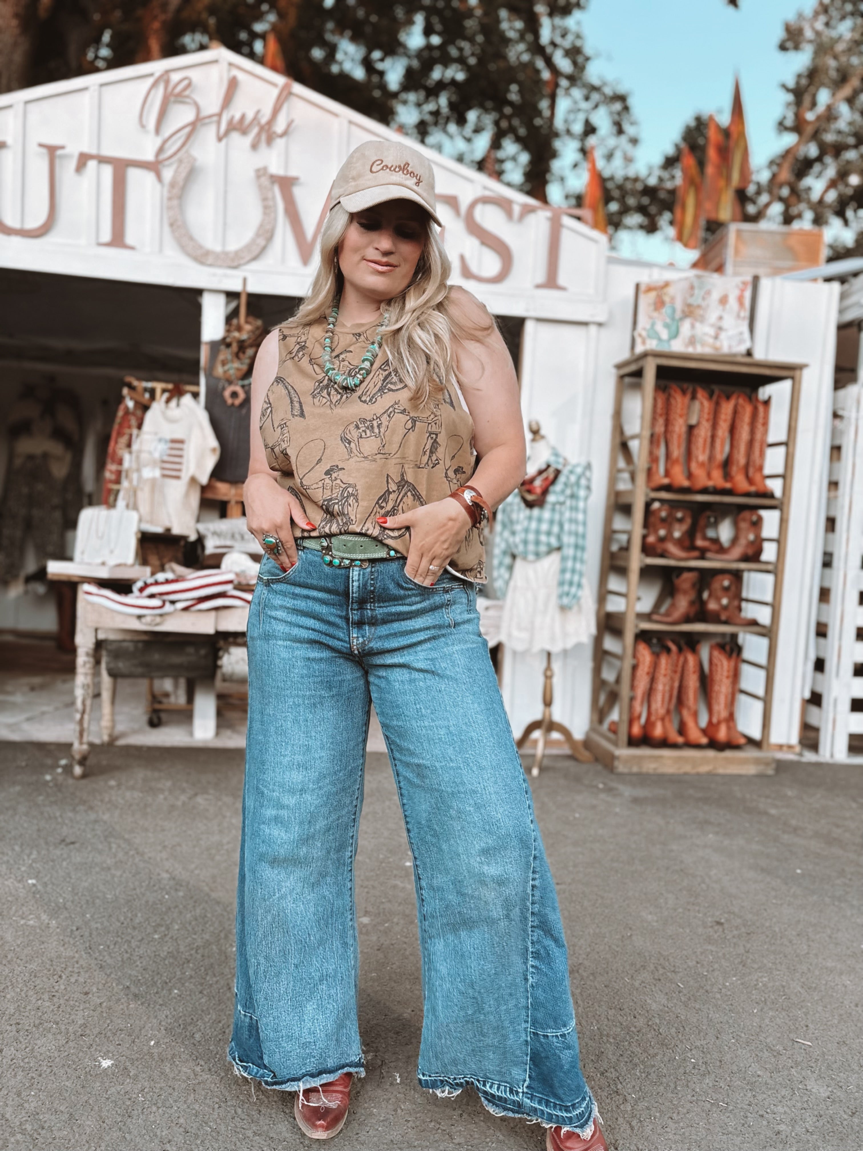 Woman in a patterned top and blue jeans standing in front of a store with cowboy boots on display.