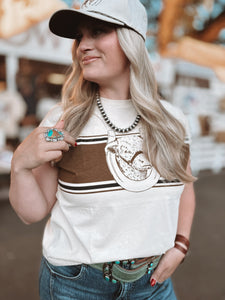 Woman wearing a white t-shirt with a graphic design, brown shirt underneath, and jeans.