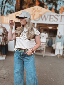 Woman wearing a white t-shirt with a graphic design and blue jeans, standing in front of a store with a 'Cowboy Western' sign.