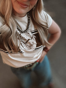Person wearing a white t-shirt with black and brown stripes, a necklace, and jeans.