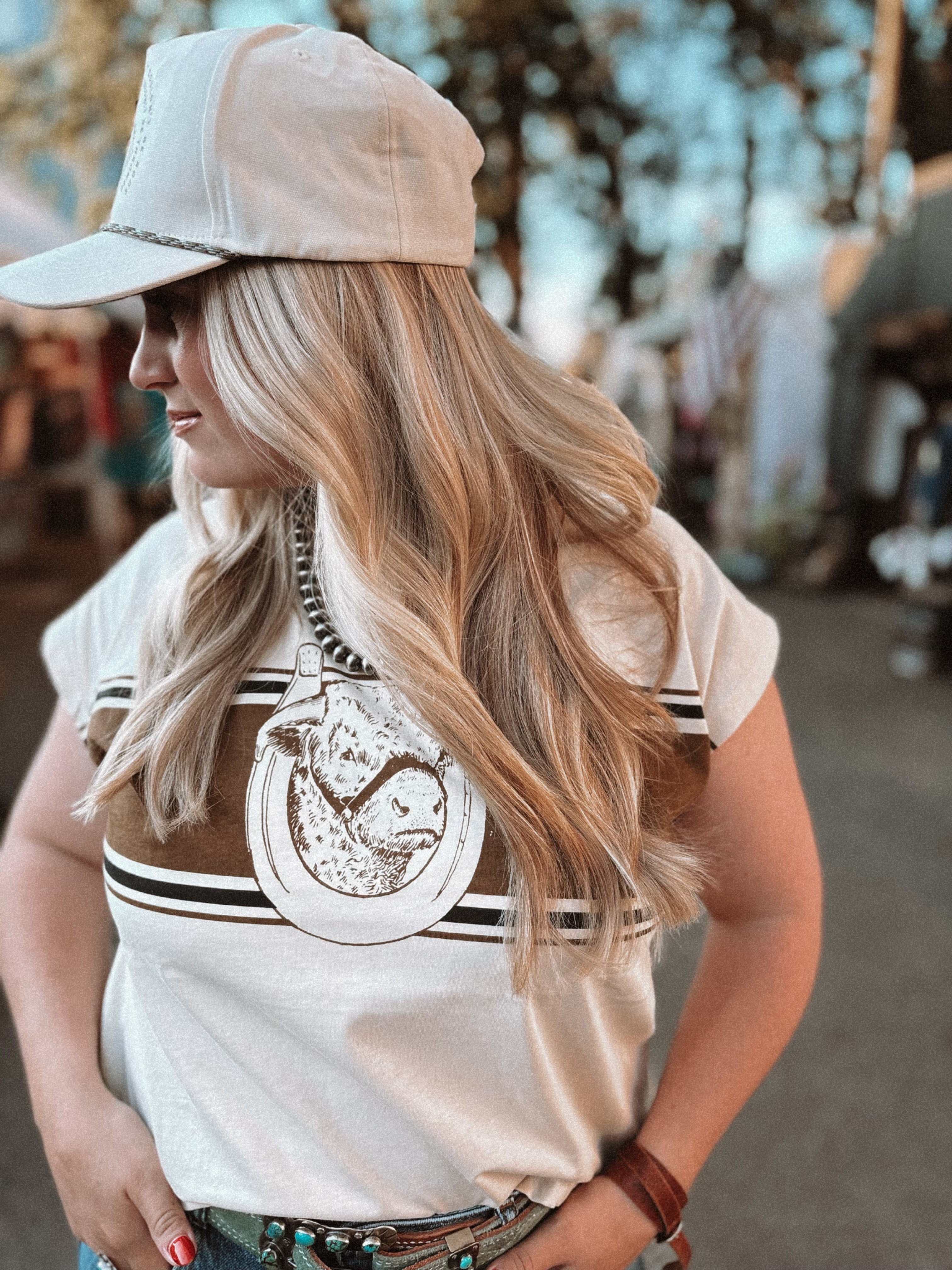 Woman wearing a beige cap and a white shirt with a logo, standing outdoors.