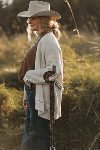 Woman in a cowboy hat and cardigan standing in a field with a blurred background