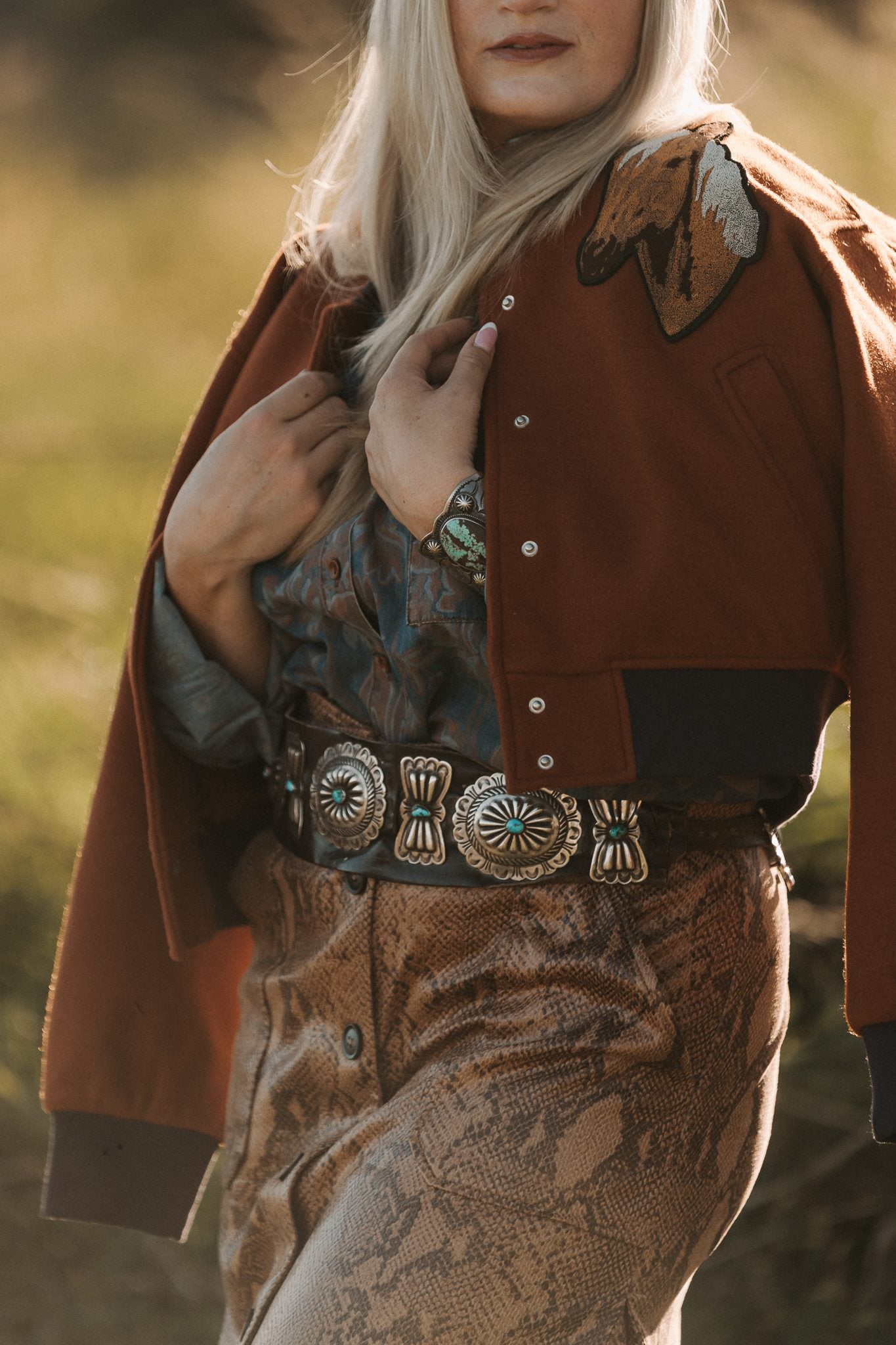 Person wearing a brown jacket with decorative buttons and patterned pants in an outdoor setting