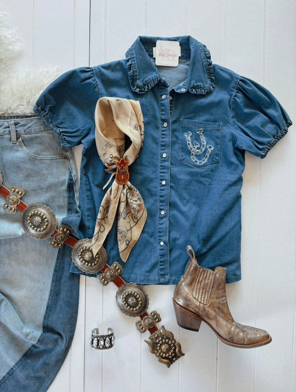 A denim button-down top with a ruffled collar and horseshoe embroidery