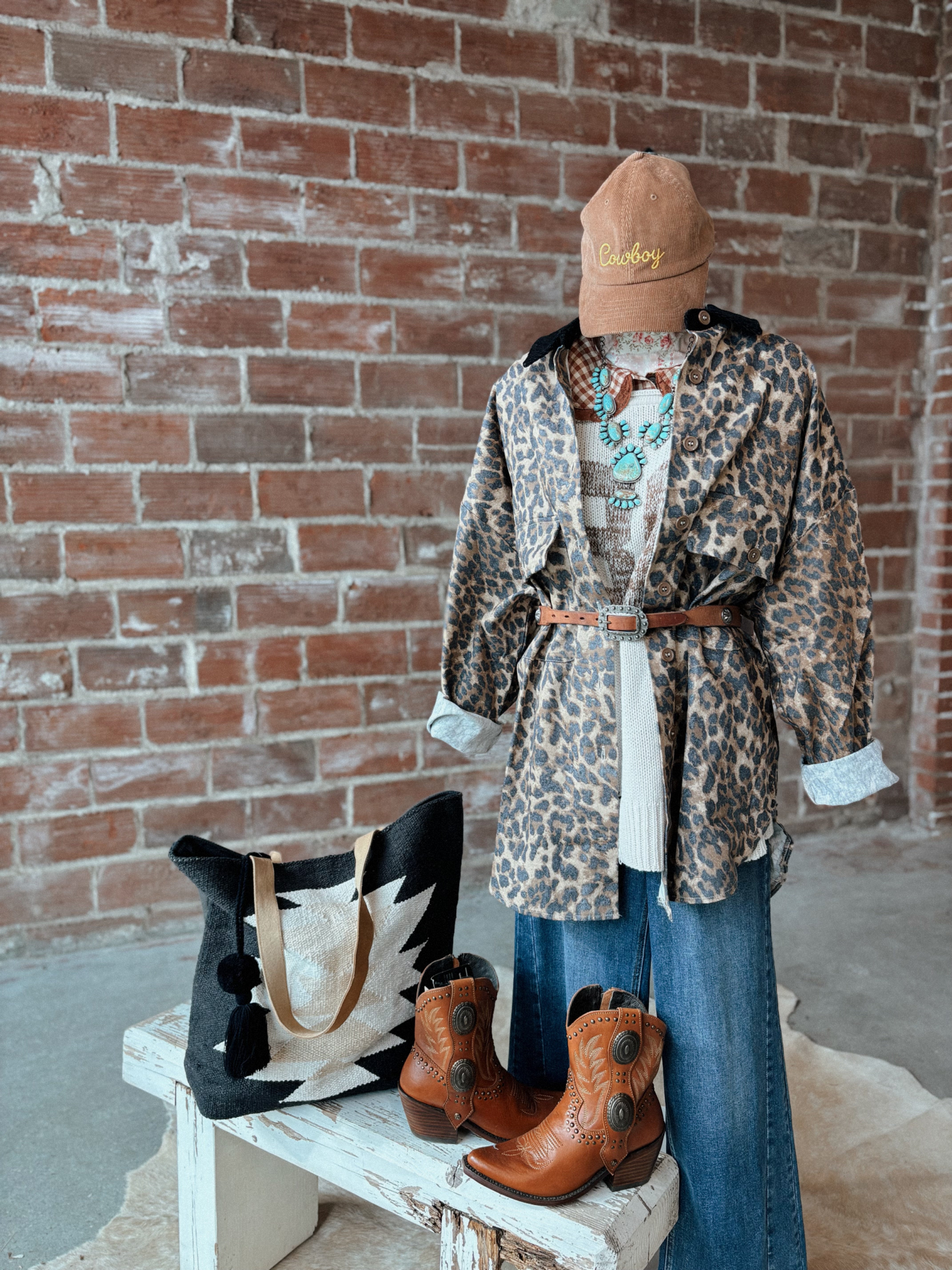 Mannequin wearing a leopard print coat, blue jeans, and brown boots against a brick wall.