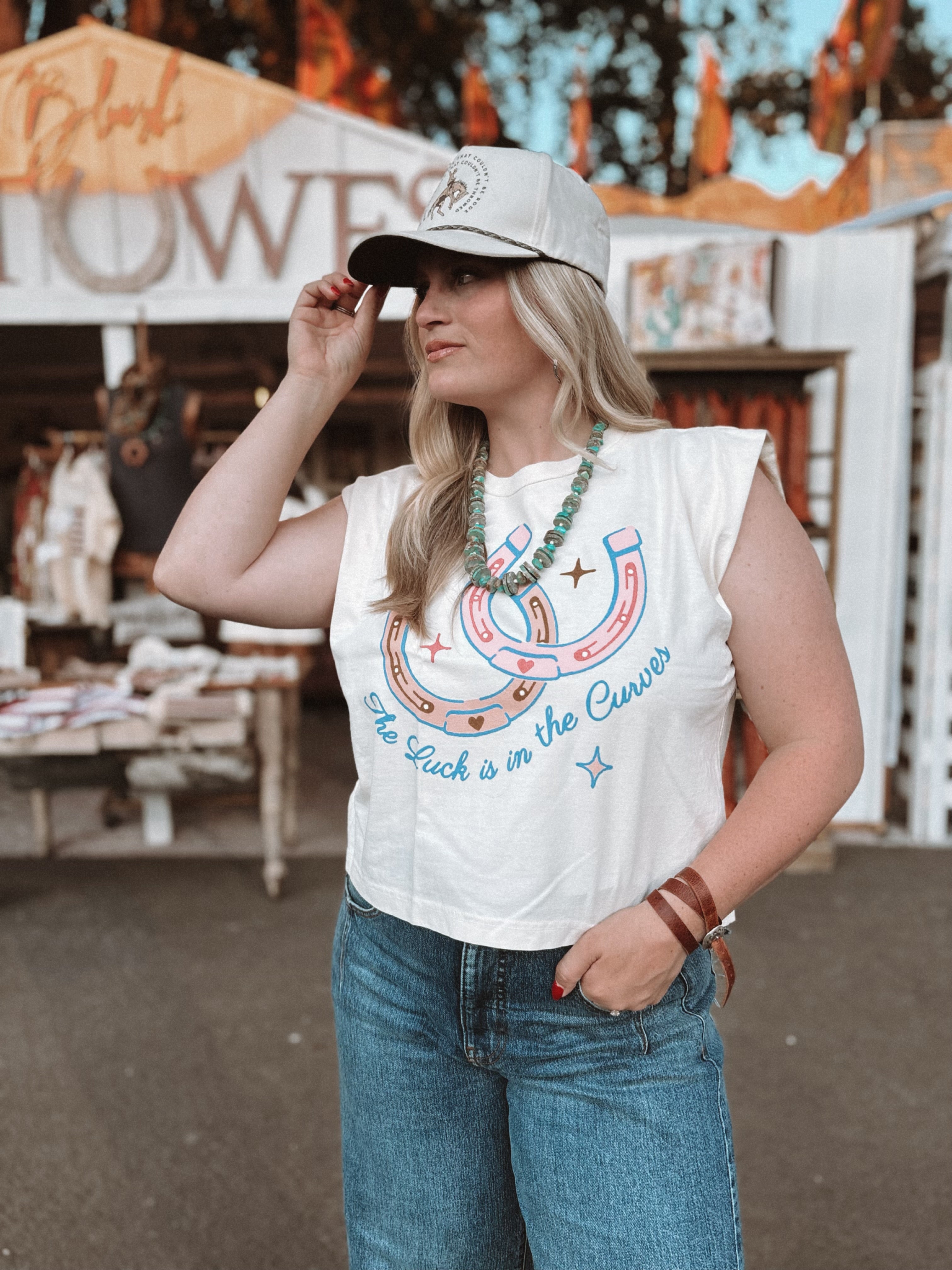 Woman wearing a white sleeveless shirt with graphic design and text, standing in front of a market stall.