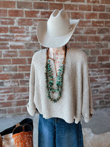 Mannequin wearing a beige sweater, blue jeans, and a white cowboy hat against a brick wall.