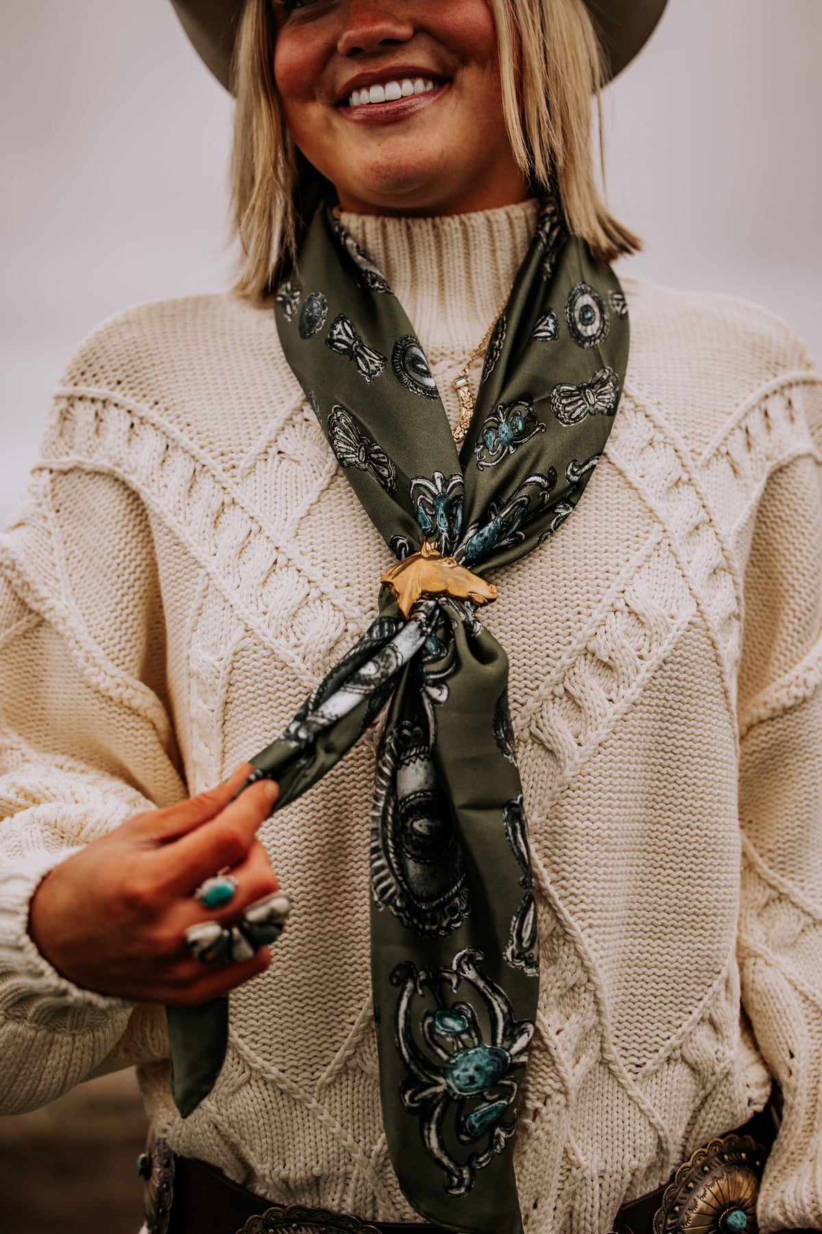 An olive silk wild rag gathered through a gold horse scarf slide