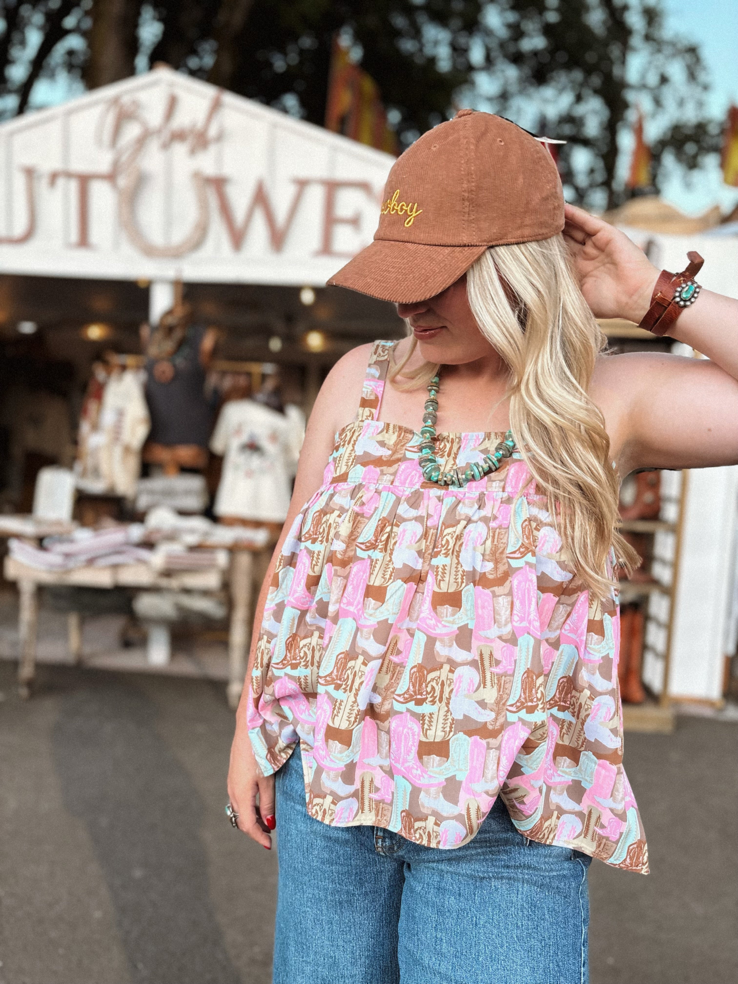 Woman wearing a boot patterned top and brown cap at an outdoor market.