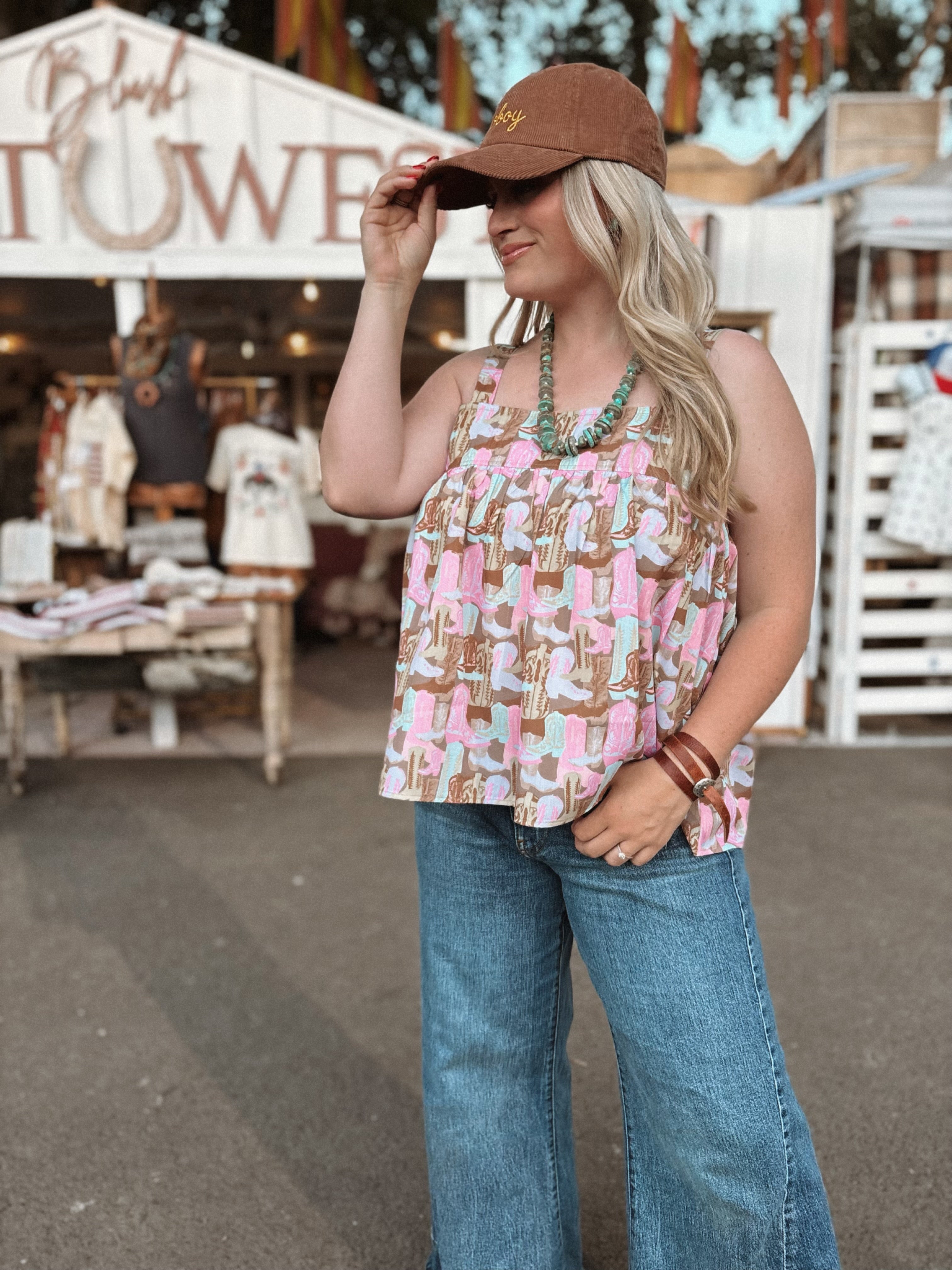 Woman wearing a patterned top and jeans with a brown cap in an outdoor setting.