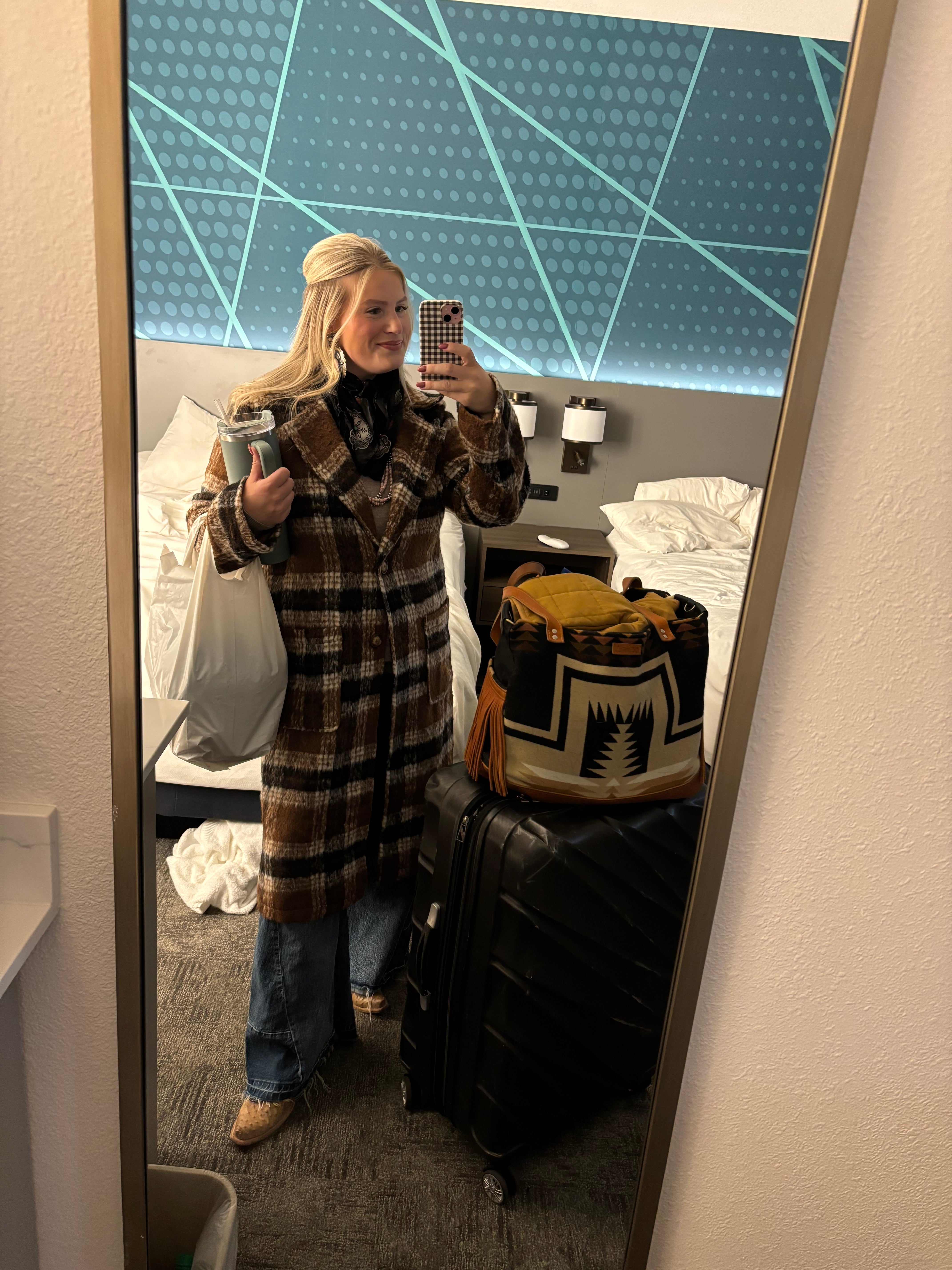 Person standing in front of a mirror wearing a plaid coat with a guitar case on the floor.