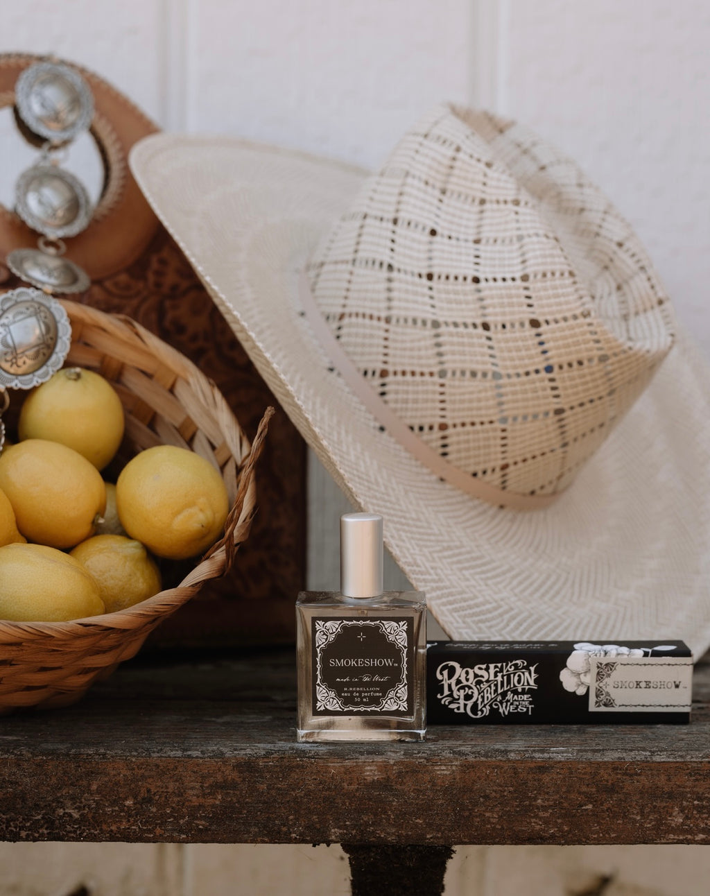 Perfume bottle and box on a wooden surface with lemons and a hat in the background