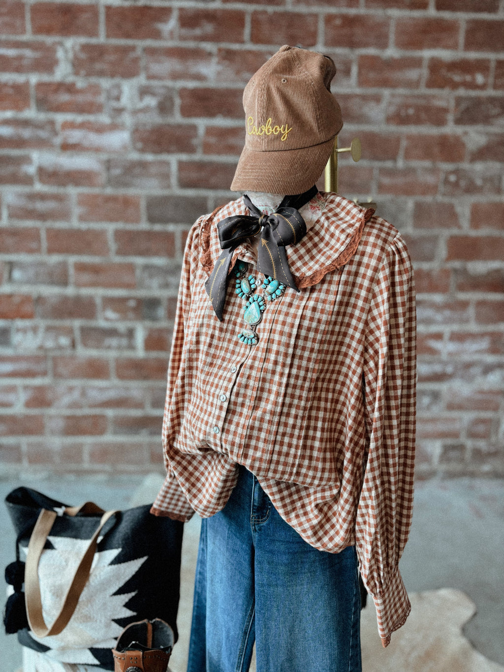 Mannequin wearing a plaid shirt, jeans, and a cowboy hat against a brick wall.
