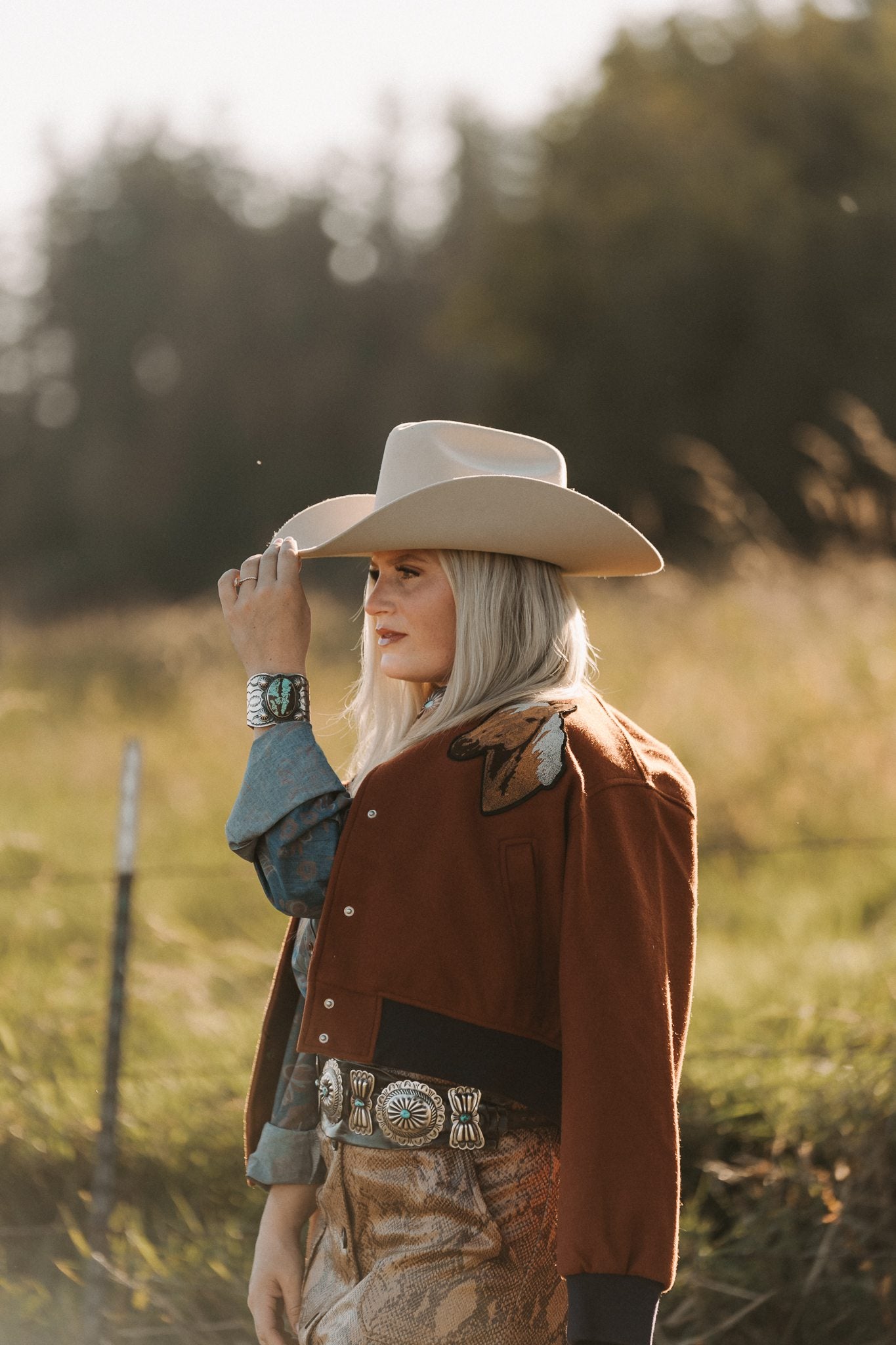Person wearing a cowboy hat and brown jacket in a field