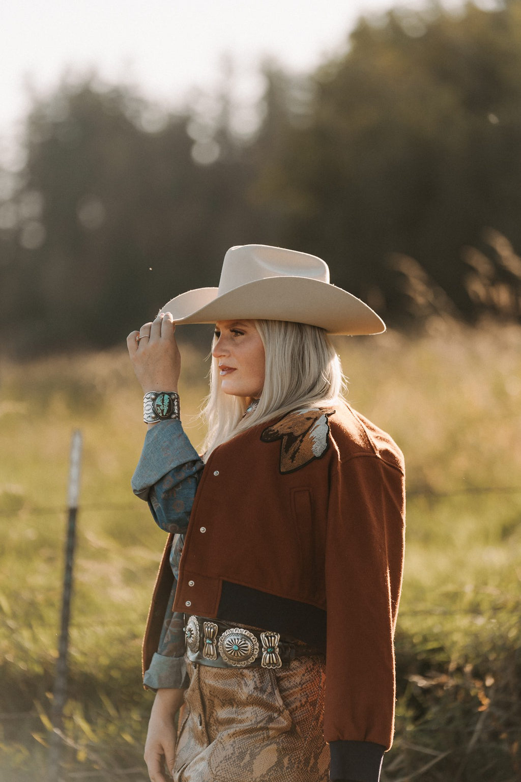 Person wearing a cowboy hat and brown jacket in a field