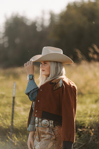 Person wearing a cowboy hat and brown jacket in a field