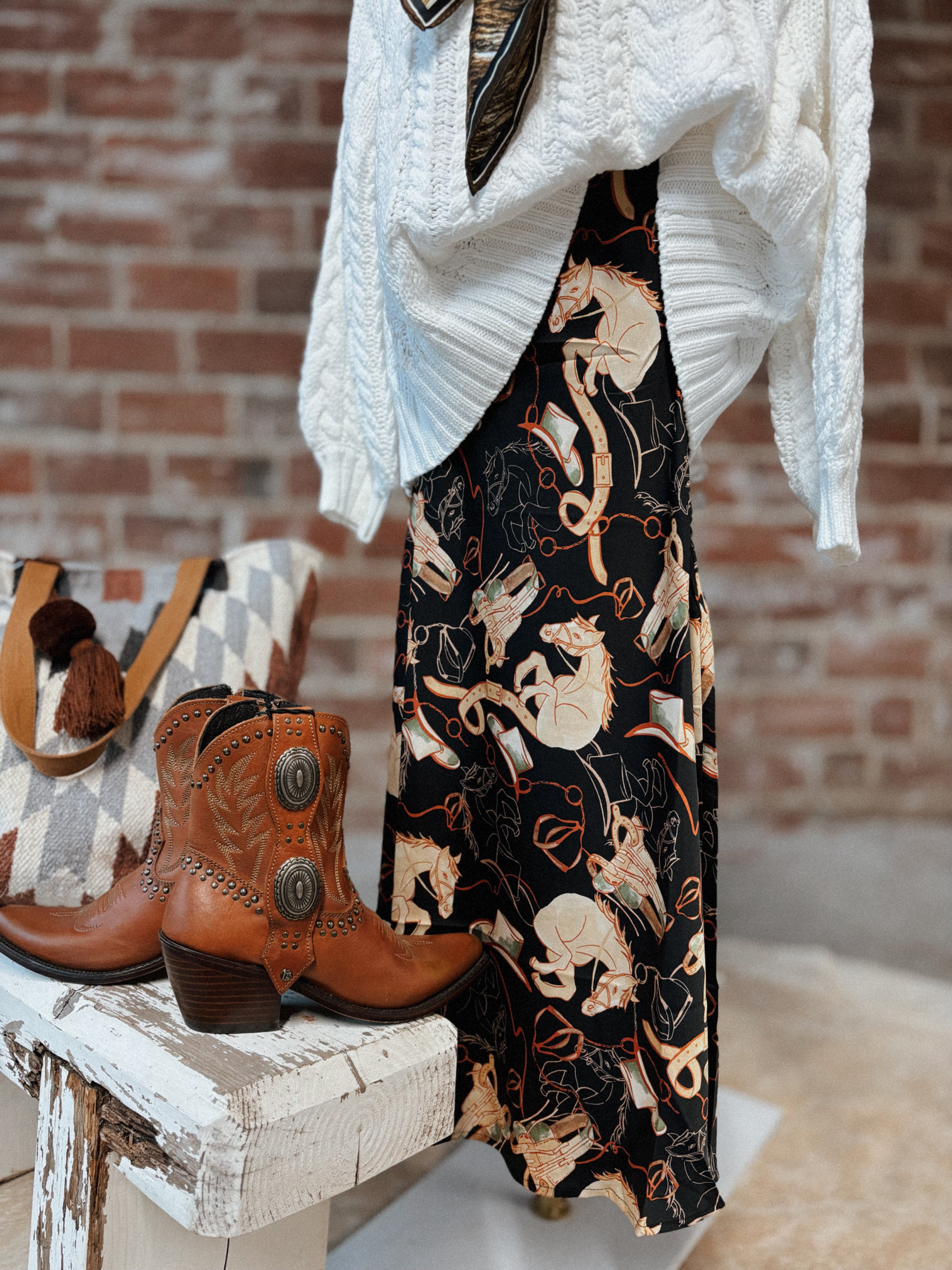 Brown cowboy boots on a white stool with a patterned skirt and white cardigan in the background.