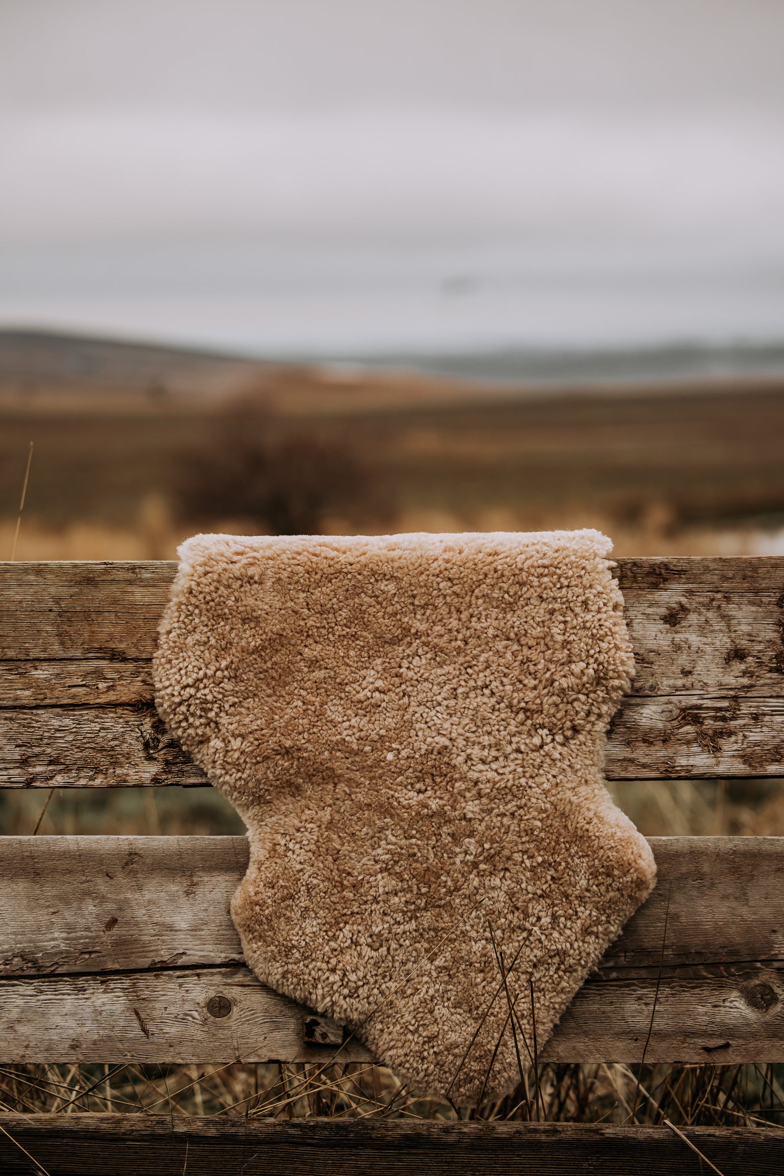 A brown sheepskin rug draped over a wooden fence with open country behind it