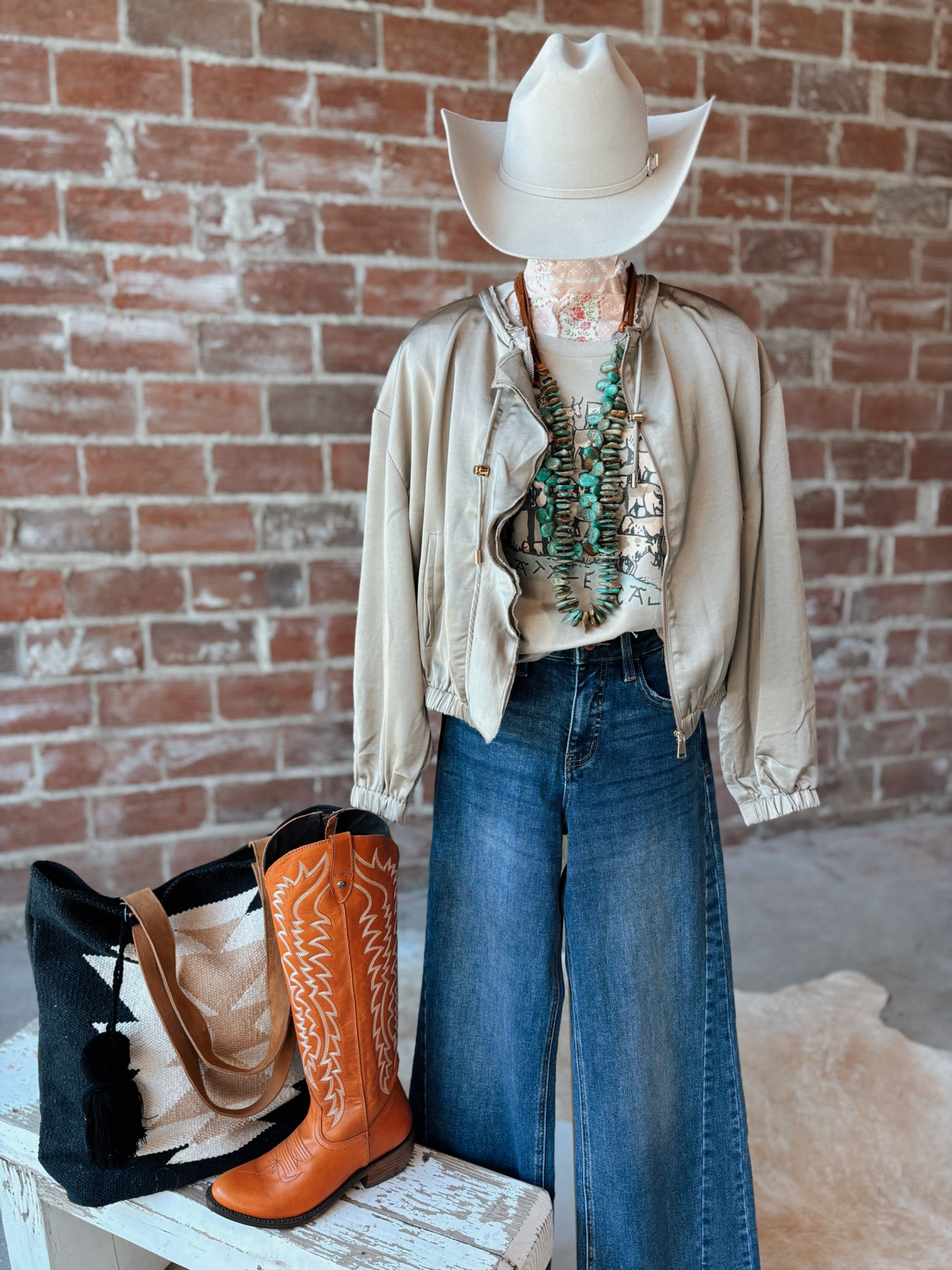 Person wearing a beige jacket, blue jeans, and orange cowboy boots with a white cowboy hat against a brick wall.