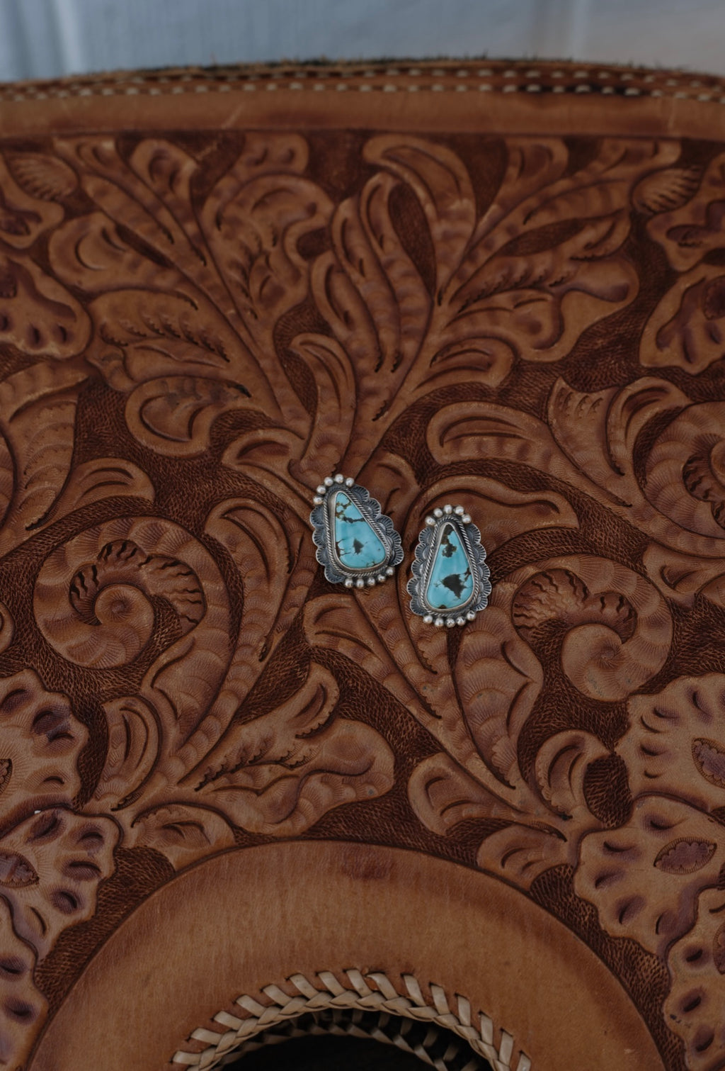 Turquoise stone earrings on a brown leather surface with intricate patterns