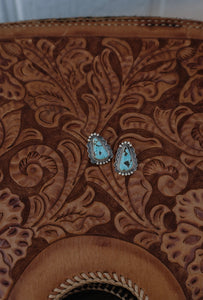 Turquoise stone earrings on a brown leather surface with intricate patterns
