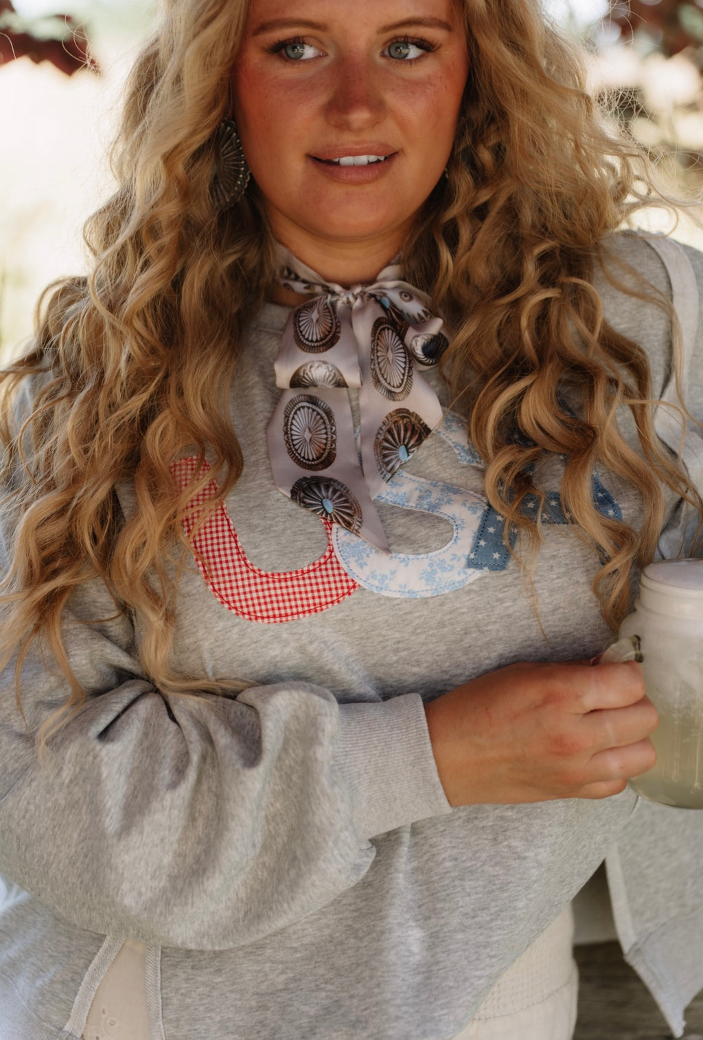 Woman wearing a gray Americana USA sweatshirt with a decorative collar, holding a mug.
