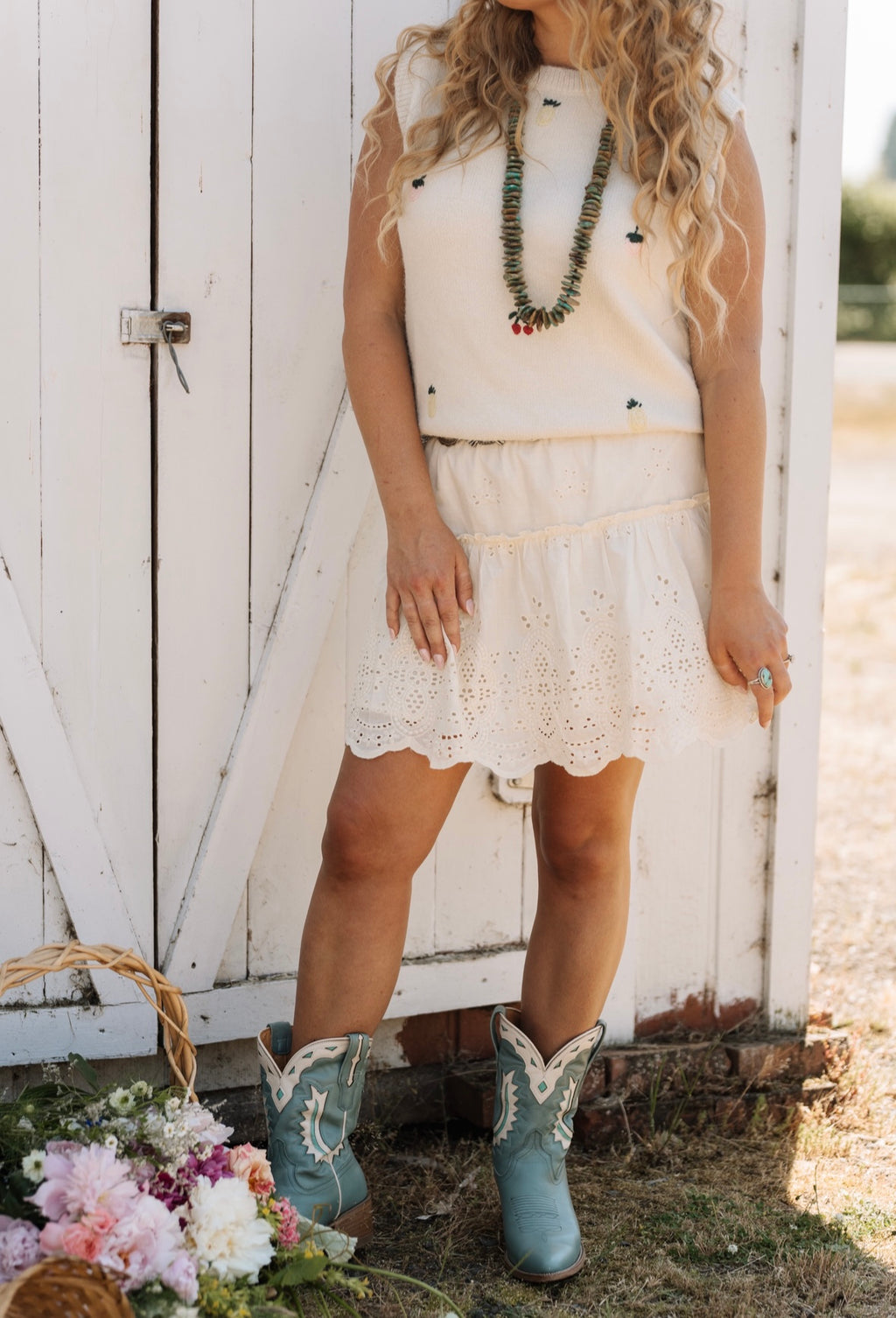 Woman wearing a white dress and blue cowboy boots standing in front of a white wooden door.