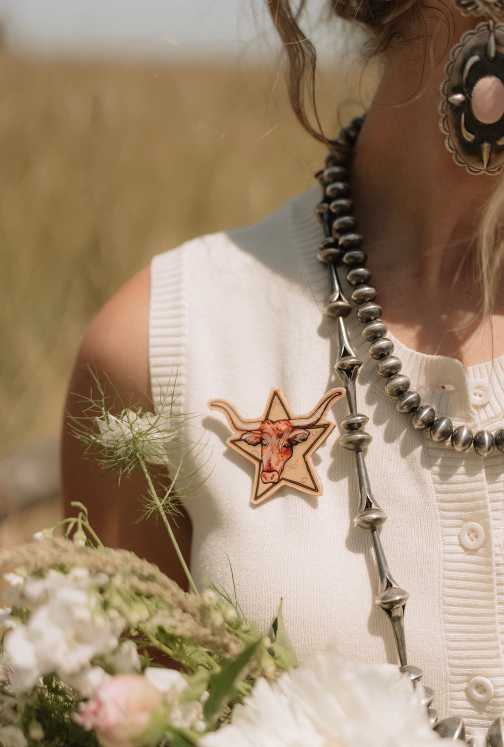 Person wearing a star-shaped Longhorn brooch and a long necklace with a blurred natural background
