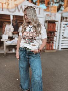 Woman wearing a graphic t-shirt and jeans standing in front of a store with outdoor decor.